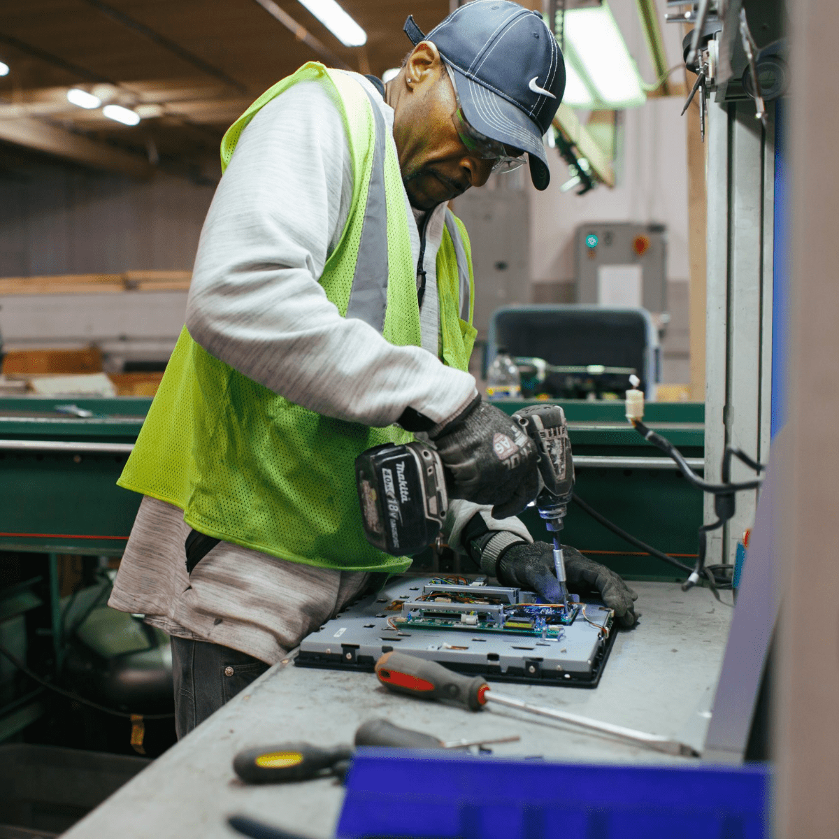 A man wearing a reflective vest using a drill to disassemble a laptop
