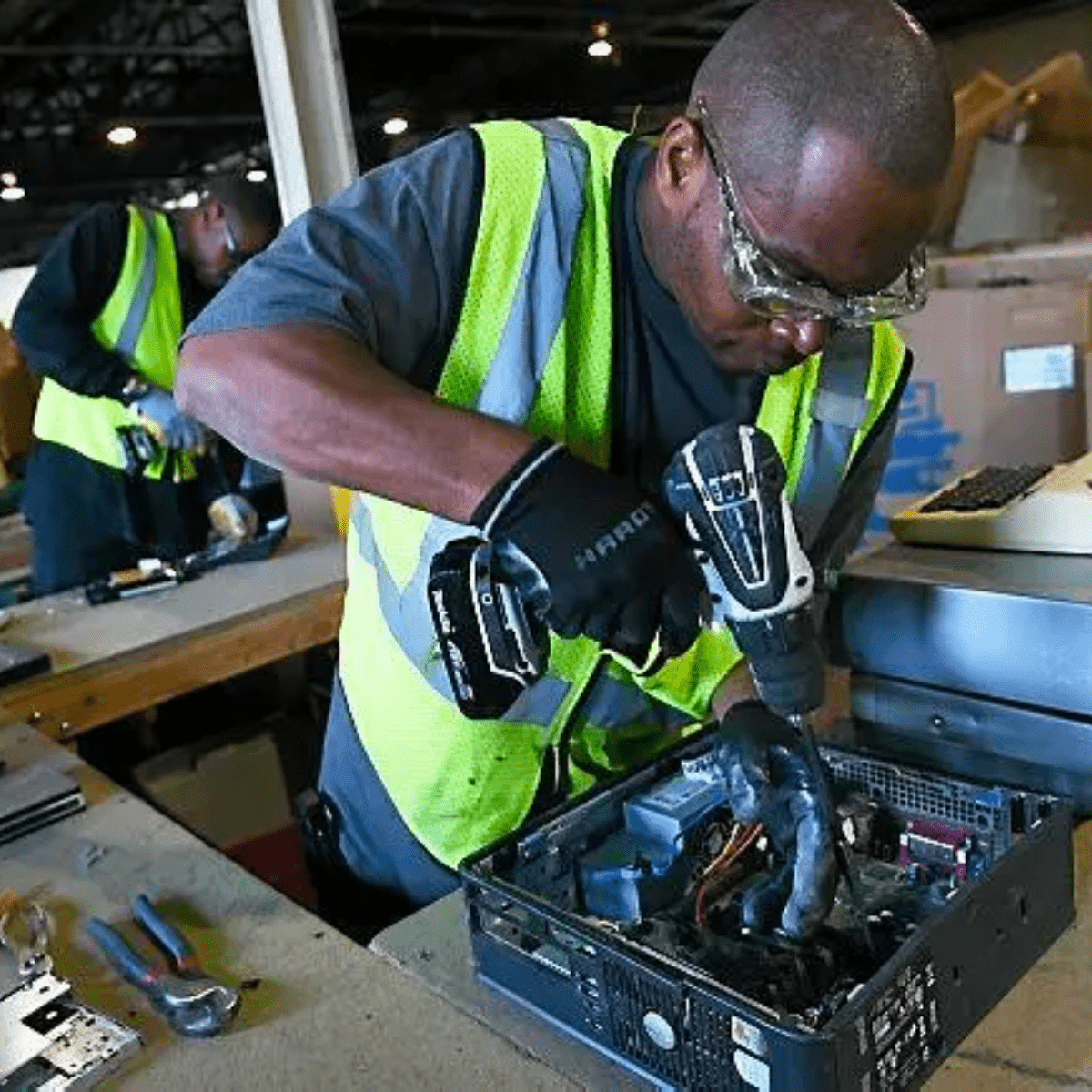 Two Black men in safety vests disassembling desktop computers
