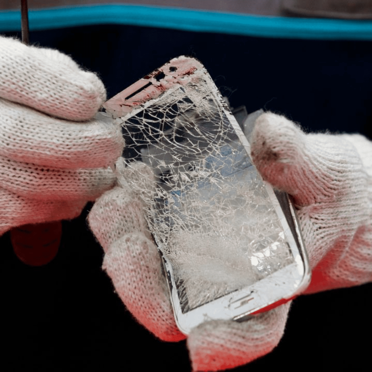 Gloved hands holding a shattered iphone