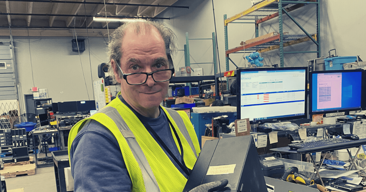 John, holding a desktop computer in Test and Repair